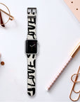 A smartwatch featuring a Love Words Vegan Leather Apple Watch Band rests on a white surface. Positioned around it are a pair of glasses, a notebook, a pen, and a paperclip. This black and white band not only displays the time but also offers an elegant and sustainable choice.