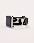 Showcasing its sustainable elegance, the smartwatch features a Love Words Vegan Leather Apple Watch Band, which highlights a unique black abstract design on a white background. Positioned at an angle on a plain, light surface, the watch's black screen adds to its refined appearance.