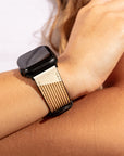 A person is wearing the Neutral Abstract Vegan Leather Apple Watch Band featuring beige and brown stripes, displayed on their left wrist. The band draws attention against a white shirt sleeve that can be partially seen within the blurred background.