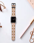 A Tan Watercolour Checker Vegan Leather Apple Watch Band rests on a white desk with office supplies, such as a gold planner, pen, paper clips, reading glasses, and a notebook. The watch face shows the time.