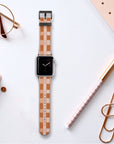 A Terracotta Watercolour Checker Vegan Leather Apple Watch Band sits on a desk surrounded by a dotted notebook, glasses, an eco-friendly pen with a grid pattern, a planner, and copper paper clips.