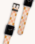 Displayed are two smartwatches featuring black faces with white and yellow hands, accented by checkered pastel orange and cream tones. They are equipped with eco-friendly Pink Checker Vegan Leather Apple Watch Bands.