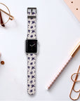 The desk holds a Wonky Stars Vegan Leather Apple Watch Band with an eco-conscious star pattern. Nearby are a notepad, gold paperclip, rose gold pen, and glasses. The minimalist scene features the watch display showing analog time with thin black hands.