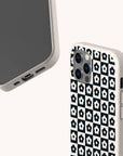 Two smartphones with white cases are displayed; one has a plain black screen, while the other showcases the Black Flower Checker Eco-Friendly Phone Case, featuring a black and white floral checker pattern and a slightly speckled texture.