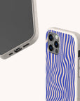 Two smartphones with beige speckled cases—one displaying the screen, the other showing the back, which features a blue and cream wavy line pattern. The Cobalt Distort Lines Eco-Friendly Phone Case is a sustainable option with precise camera and port cutouts, compatible with both iPhone and Samsung Galaxy models.