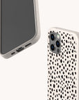 Two smartphones are displayed, one showing the front and one the back. The Dark Spots Eco-Friendly Phone Cases, compatible with both iPhone and Samsung Galaxy models, feature a minimalist white background adorned with black speckles reminiscent of a dalmatian pattern. The cases showcase a triple camera cutout and clearly visible side buttons.