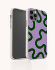 A smartphone fitted with the Purple and Green Swirl Eco-Friendly Biodegradable Phone Case, which features a wavy green pattern on a lavender background, is displayed from both the front and angled rear view.