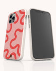Two smartphones in beige, each featuring the Red and Pink Swirl Lines Eco-Friendly Phone Case—a case compatible with both iPhone and Samsung. One phone displays the distinctive pink and red swirling line design, while the other shows a blank black screen. Both phones stand upright on a white background.
