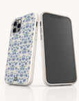 Two smartphones with white cases are shown; one features the Blue Ditsy Flowers Eco-Friendly Biodegradable Phone Case, while the other displays its screen. Both cases have a smooth finish and rounded edges.