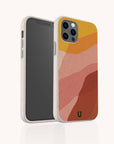The Cliffs Eco-Friendly Phone Case, shown on a smartphone, features a beige textured abstract design with wavy orange, pink, and red layers in warm earth tones. Compatible with iPhone and Samsung Galaxy; front and back views are visible.