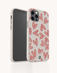 A smartphone in a Pink Hearts Eco-Friendly Biodegradable Phone Case, featuring a pattern of red hand-drawn hearts on a beige background. The phone stands upright with the back and side of this sustainable accessory visible against a plain white backdrop.