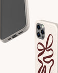 The Brown Bow Ribbon Eco-Friendly Phone Case features a beige speckled design with a large abstract brown bow ribbon, visible camera lenses and buttons, blending style and sustainability.