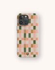 The Pink and Green Watercolour Eco-Friendly Phone Case features a pink, peach, green, and tan checkerboard pattern with a small black horseshoe logo at the bottom center.