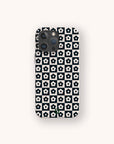 A smartphone with the Black Flower Checker Eco-Friendly Phone Case, featuring a black and white checker design of white flowers with black centers, is shown from the back on a light background.