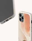 Two smartphones with abstract, pastel-colored cases are displayed. One phone reveals the screen, while the other showcases the back featuring the Pink and Brown Watercolour Eco-Friendly Phone Case, adorned with peach, tan, and cream accents. Both devices rest against a plain backdrop, emphasizing the sleek design and sustainable construction of these plant-based cases.