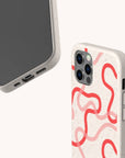 Two smartphones with Pink and Red Swirls Eco-Friendly Biodegradable Phone Cases are shown. The cases feature red abstract swirls on a beige, eco-conscious material. One phone displays the screen and charging port, while the other highlights the back design and side buttons. Both phones are set against a light background.