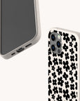 Two smartphones with speckled white cases are displayed; one reveals its screen and bottom ports, while the other showcases the back adorned with the Black Flower Power Eco-Friendly Phone Case—a chic black floral pattern. Both stylish devices rest against a plain light background, blending modern elegance with the retro charm of the Black Flower Power Eco-Friendly Phone Case.