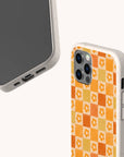 Two smartphones in beige cases are displayed; one shows its screen, while the other reveals the back featuring the Orange Flower Check Eco-Friendly Phone Case, which has rounded edges and precise cutouts for buttons, ports, and the camera.