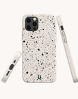 The Black Splatter Eco-Friendly Phone Case is displayed from three angles—back, side, and bottom—highlighting its speckled white design with black spots. Designed to fit an iPhone with triple rear cameras, it features a small green horseshoe logo. Both stylish and sustainable, this compostable phone case offers eco-conscious protection without sacrificing design.