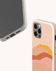 Two views of the Hills Eco-Friendly Phone Case in speckled beige with an abstract wavy design in pastel pink, orange, and yellow. Shown from front and back; compatible with iPhone and Samsung Galaxy models.