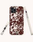 Three views of the Brown Cow Print Eco-Friendly Phone Case, featuring a green horseshoe logo, white sides with accessible buttons and ports, and compatible with iPhone and Samsung Galaxy devices.