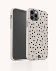 The Black Hearts Eco-Friendly Phone Case is beige with a scattered black heart pattern, covers the back and sides of your smartphone, and features cutouts for camera lenses and buttons. The case is biodegradable.