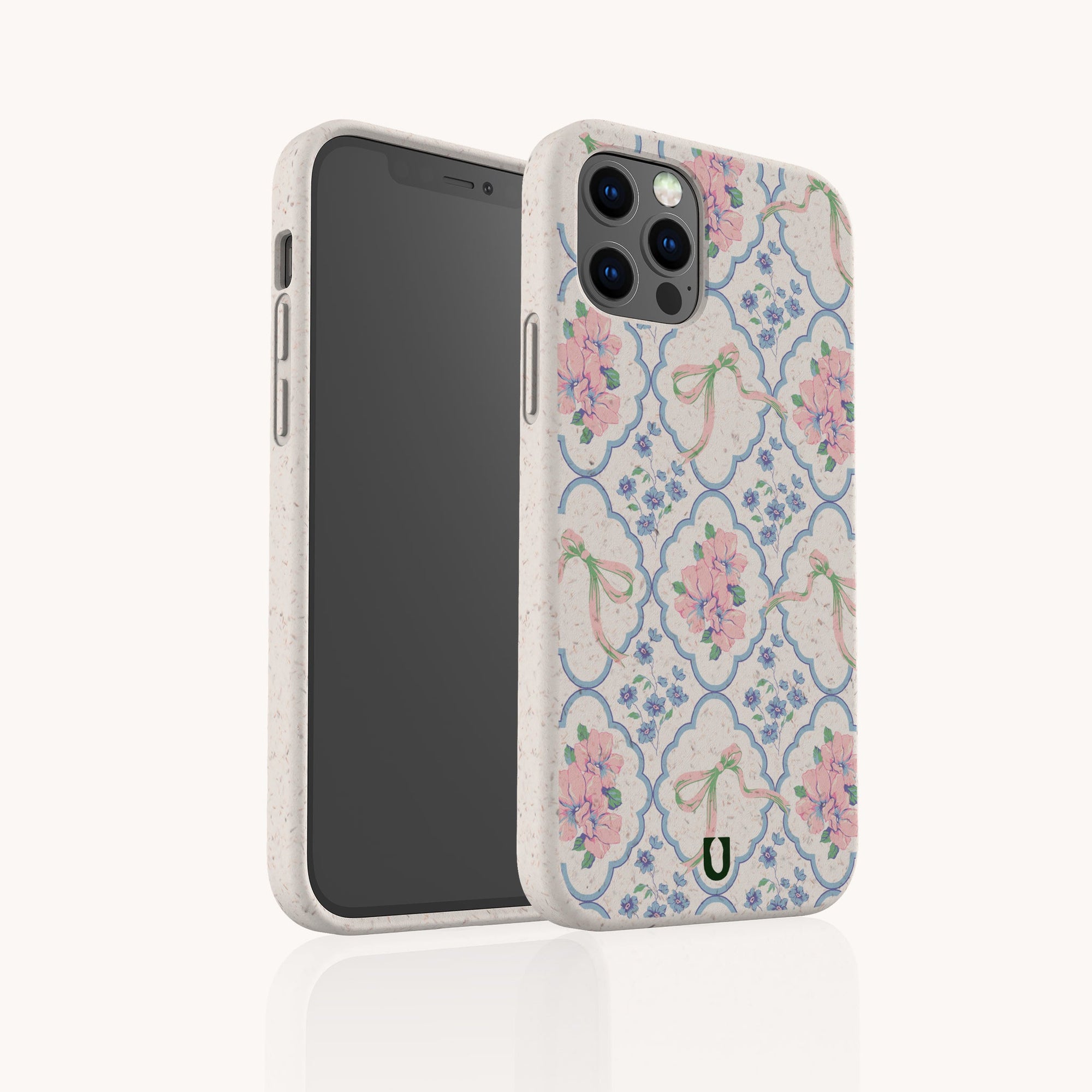The Pink Ribbons Eco-Friendly Biodegradable Phone Case, featuring pink flowers, green ribbons, and blue lattice on white, is shown upright beside a smartphone, displaying both the floral design and the eco-conscious material.
