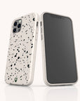 Two smartphones with Black Terrazzo Eco-Friendly Phone Cases—one showing the screen, the other displaying the back with three camera lenses and a small green shield logo—stand upright on a white reflective surface.