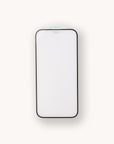 A black rectangular Eco Glass Screen and Camera Lens Protector lies face down on a light surface, highlighting its sleek design. The eco-friendly back, made of recycled tempered glass, is white with "TOP" at the top and a faint blue circle visible.
