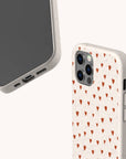 Two smartphones with beige cases: one, the Red Hearts Eco-Friendly Phone Case, features a repeating red heart pattern, while the other—displayed as a Samsung Galaxy case—shows the phone screen and charging port. Both cases have a smooth, matte texture.
