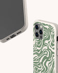 Two smartphones with beige-speckled, sustainable cases are shown on a light background. One phone features the Green Marble Swirl Eco-Friendly Phone Case, displaying a green and white abstract wavy pattern reminiscent of marble; the other case is plain. Both highlight the camera and charging ports.