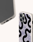 Two smartphones in beige Speckled Swirl Eco-Friendly Biodegradable Phone Cases: one reveals the screen and charging port, while the other shows off the back’s wavy black and blue dot pattern. Both cases feature rounded edges with precise cutouts for buttons and cameras.