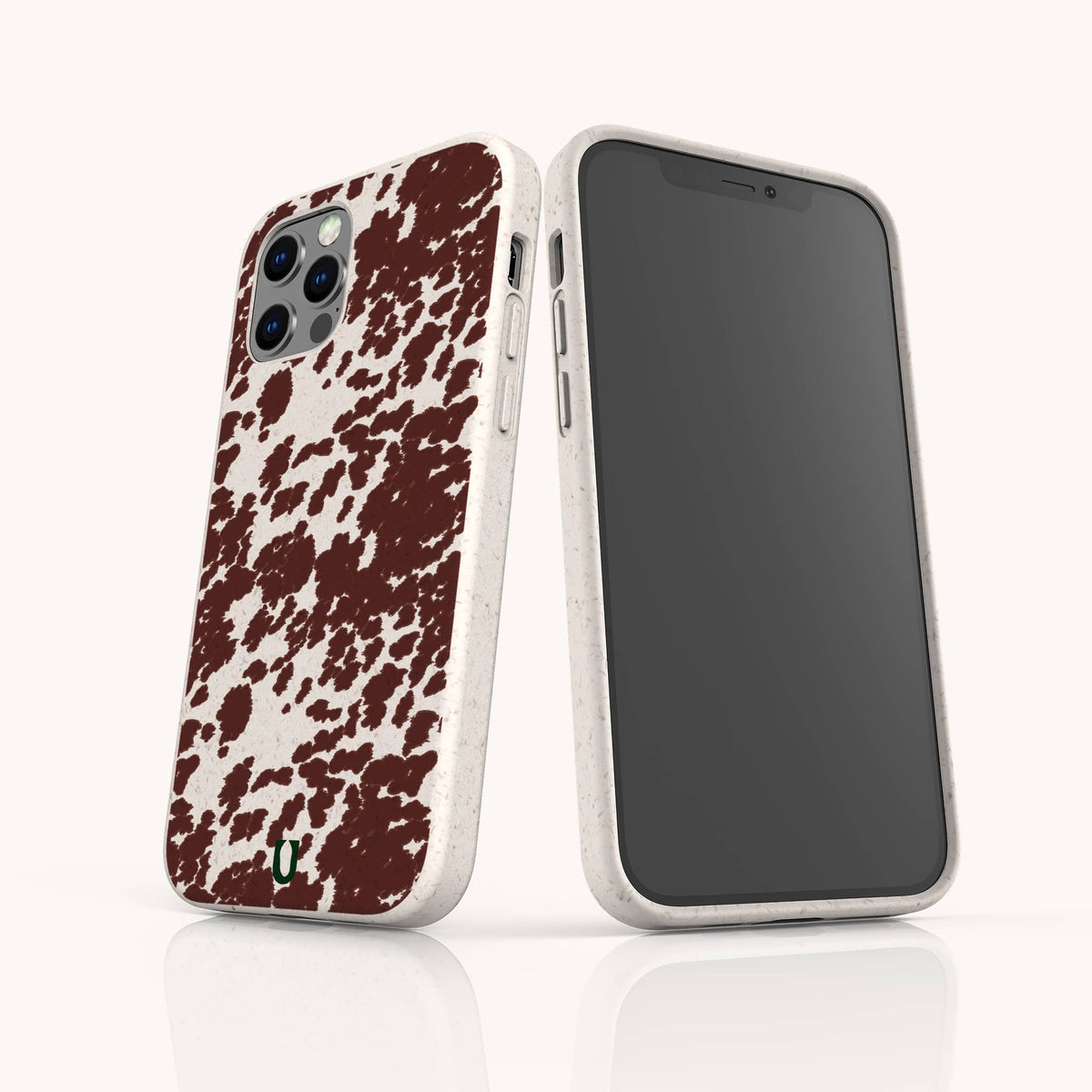 Two smartphones with matching Brown Cow Print Eco-Friendly Phone Cases are displayed. The off-white cases feature a brown cow print pattern on the back and precise camera cutouts. One phone, an iPhone, is shown facing forward, while the other, a Samsung Galaxy, displays the back of its case.