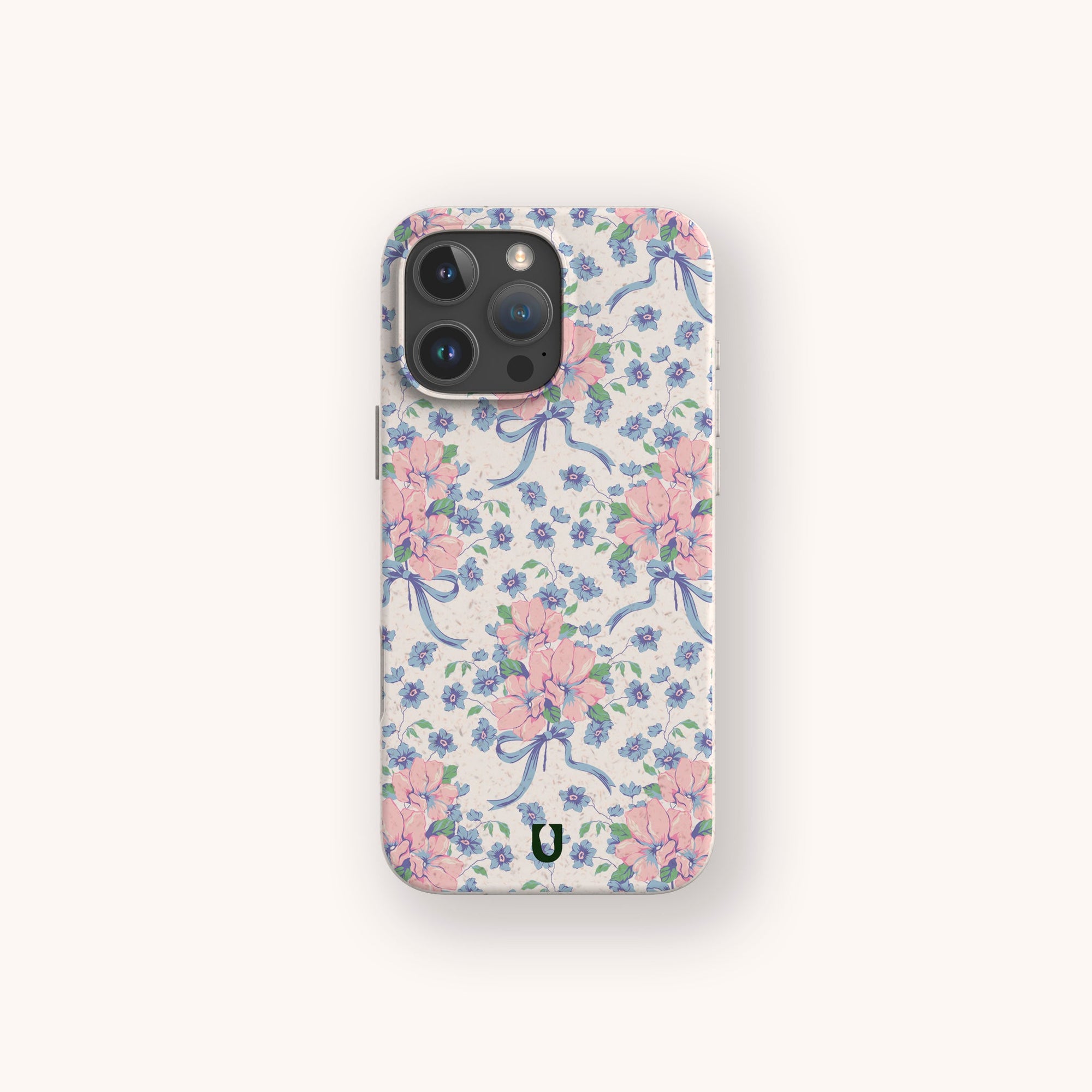 The Pink and Blue Coquette Flowers Eco-Friendly Biodegradable Phone Case features pink flowers, blue ribbons, and small blue flowers on a light background, shown against an off-white surface.
