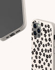 Here’s a rewritten version using the provided product name: Two views of a smartphone fitted with the Little Black Flowers Eco-Friendly Biodegradable Phone Case, featuring a beige design adorned with small black flower patterns. The case protects the back and sides of the phone, which has a triple camera setup. The background is plain and light-colored.
