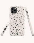 Three views of a smartphone in the Black Terrazzo Eco-Friendly Phone Case, featuring a light beige, speckled terrazzo-style design with black and gray flecks. The images display the back, side, and bottom of the phone against a plain background. This stylish case is both compostable and eco-friendly, offering protection while supporting sustainability.