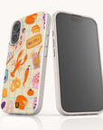 Two smartphones with white cases are displayed; one features the Taste of Summer Eco-Friendly Biodegradable Phone Case, which showcases a colorful and whimsical food-themed design with a lobster, pretzel, bread, and various kitchen items on a tiled background. This case is crafted from sustainable materials. The second phone’s screen is turned off.