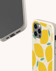 Two smartphones with beige speckled cases—one featuring the Lemons Eco-Friendly Phone Case, which displays a vibrant yellow lemon and green leaf design. The phones are positioned to reveal both the front and back views against a plain light background.