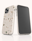 Two smartphones are shown with Brown Terrazzo Eco-Friendly Phone Cases—one facing front, one back. The compostable cases feature a terrazzo-style design with multicolored speckles, precise cutouts for the camera and buttons, and a small green horseshoe logo at the bottom.