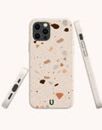 Three views of a smartphone in the Terrazzo Print Eco-Friendly Phone Case, showcasing its beige surface with multicolored specks. This case features precise camera and button cutouts, plus a small green horseshoe-like logo at the bottom.