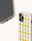 Two smartphones in speckled beige cases are displayed against a plain light background; one showcases the Pastel Checker Biodegradable Eco-Friendly Phone Case featuring a sustainable design with pastel yellow, green, and pink checks, while the other shows the blank screen side.