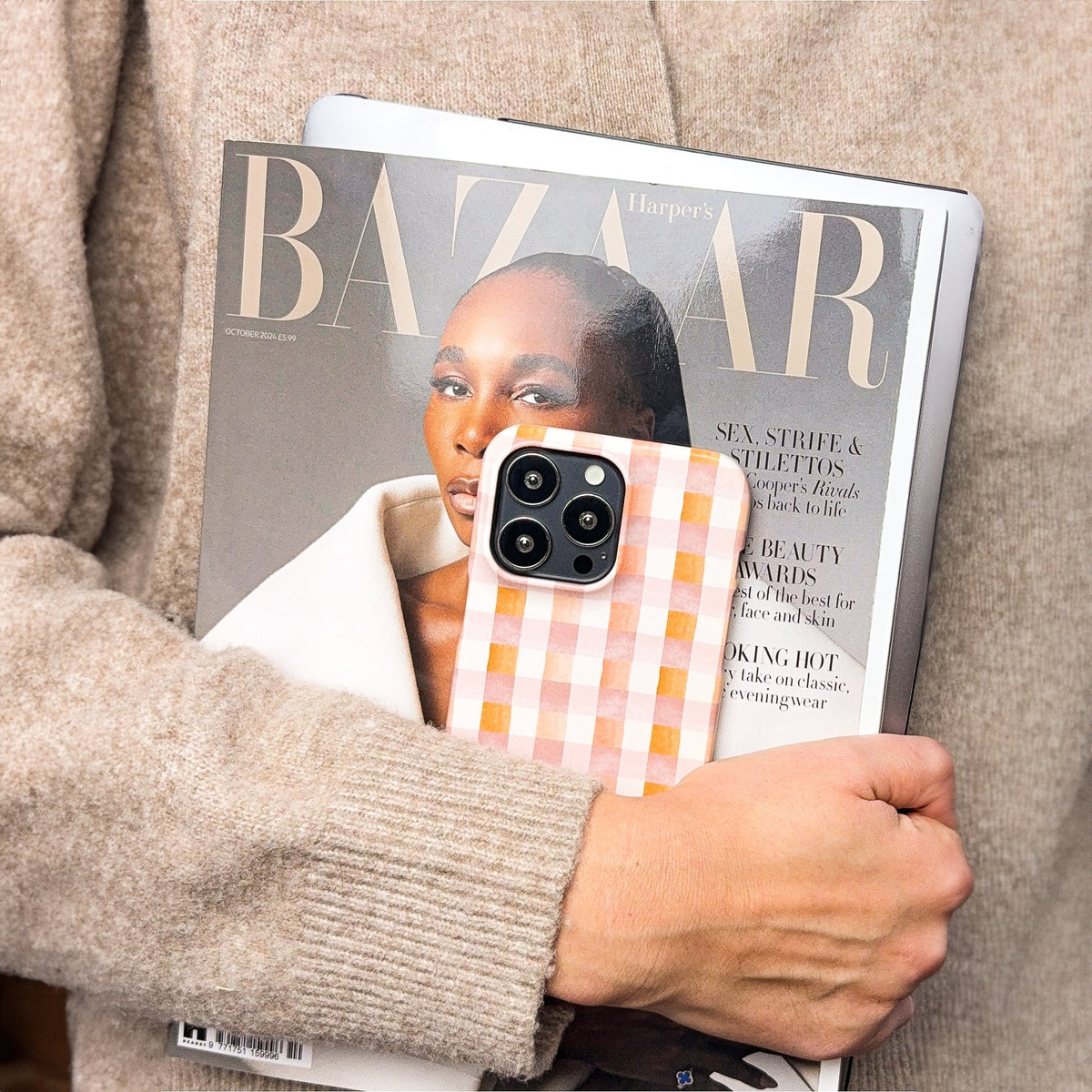 A person in a beige sweater holds a Harper’s Bazaar magazine and a tablet, with a Pink and Brown Gingham Eco-Friendly Phone Case visible in their hand.