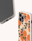 Two phones in speckled beige cases; one phone faces forward, while the other displays the Orange Blossom Eco-Friendly Phone Case featuring illustrated oranges, white blossoms, and green leaves on a light background.