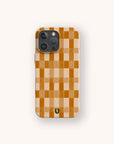 A smartphone is shown with the Brown Watercolour Checker Eco-Friendly Phone Case, which features a brown checker pattern and a small green horseshoe symbol at the bottom center. The case complements the device’s three rear cameras and is displayed against a light background.