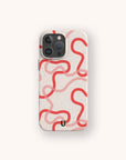 A Pink and Red Swirls Eco-Friendly Biodegradable Phone Case in white, displaying a pattern of wavy, interconnected red lines and a small black curved mark near the bottom, is shown on a smartphone set against an off-white background.