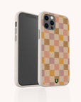 A smartphone in the Pink and Purple Checker Eco-Friendly Phone Case, featuring a white speckled, biodegradable design with a pink, beige, and tan checkerboard pattern on the back. A small green logo is located near the bottom of the case, and the phone screen is turned off.