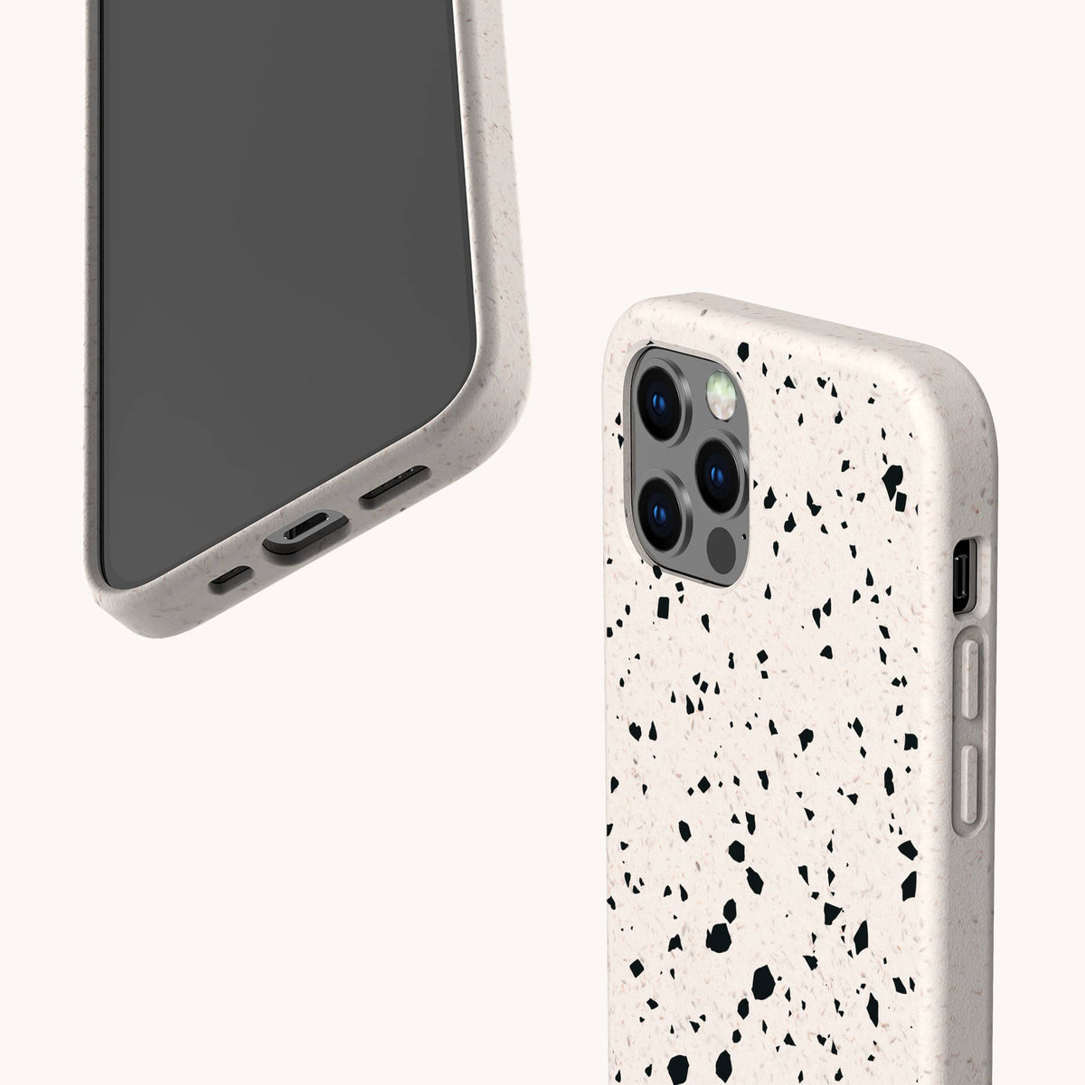 Two smartphones in Black Terrazzo Eco-Friendly Phone Cases—speckled off-white with black spots—are shown from different angles against a light background, showcasing the camera modules and the unique case texture.
