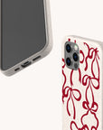 Two smartphones are shown in beige speckled protective cases. One case is plain, while the other is the Burgundy Bow Ribbons Eco-Friendly Phone Case, featuring a red abstract bow pattern. Both biodegradable phone cases are angled to display the screen, charging port, buttons, and camera lenses.