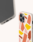 Two views of the Paper Scraps Eco-Friendly Biodegradable Phone Case, featuring a colorful abstract geometric pattern with pink, orange, yellow, and brown shapes. One view displays the smartphone’s front and bottom ports, while the other highlights the back design and camera.