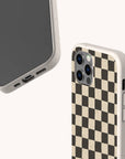 Two smartphones with beige-speckled cases; one showcases the Black Checker Eco-Friendly Phone Case, featuring a bold black-and-beige checkerboard design on the back, while the other shows its front screen and charging port. Both provide an eco-friendly option for sustainable style.